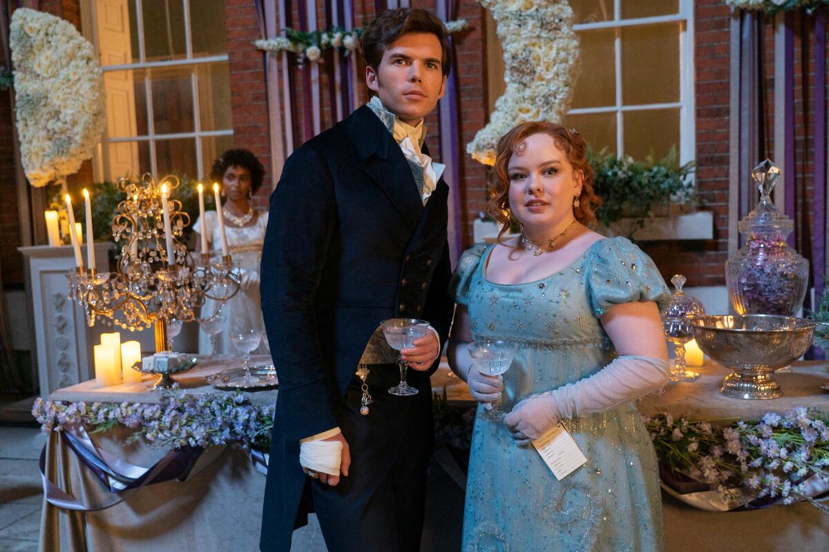 A man and a woman in Regency-era wardrobe stand in front of an ornately decorated tablescape