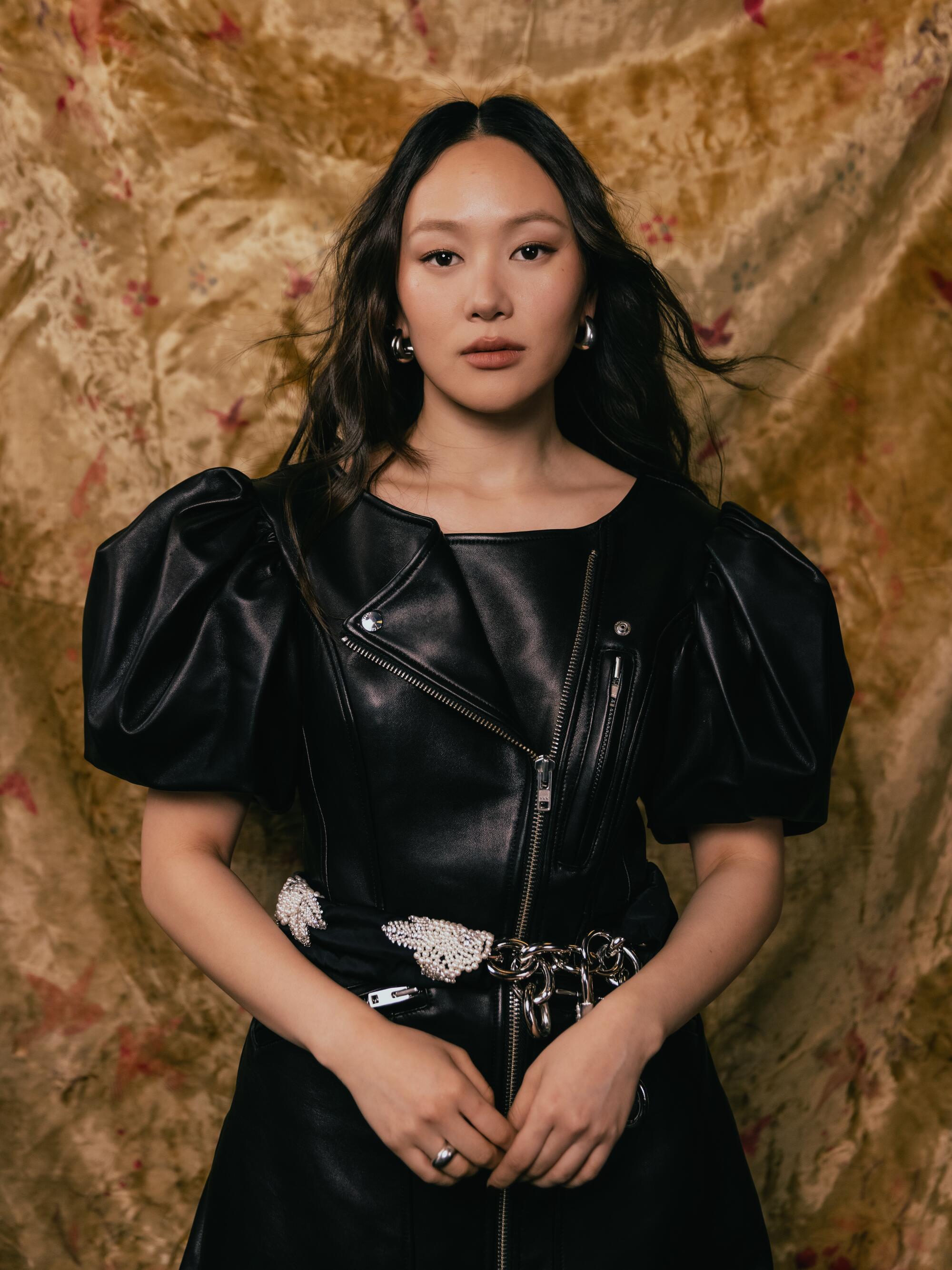 A woman in a black dress poses against a backdrop