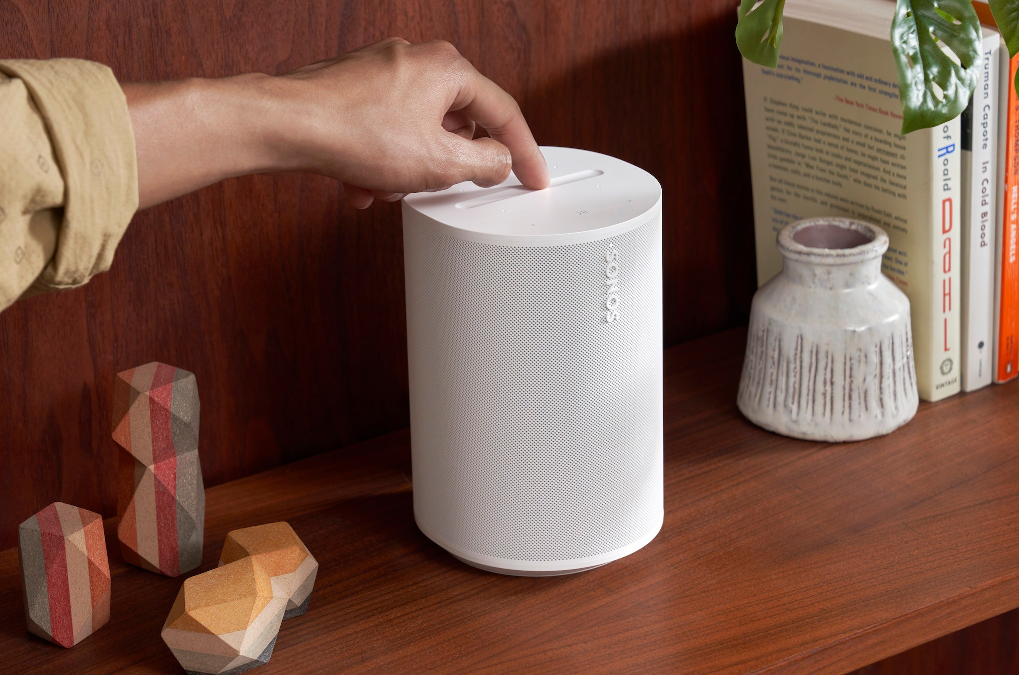 A marketing image of the Sonos Era 100 speaker on a wood shelf.