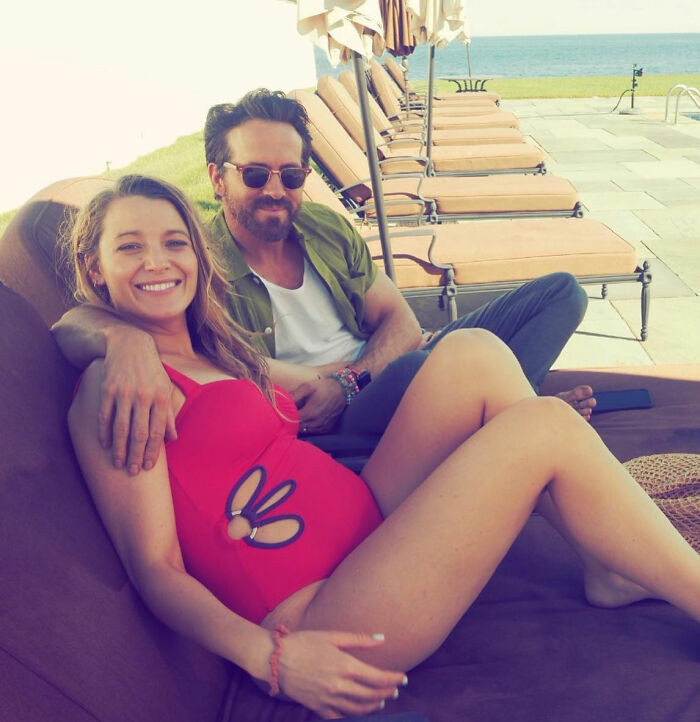Blake Lively and a man relaxing by the pool on lounge chairs with ocean in the background, casual summer setting.