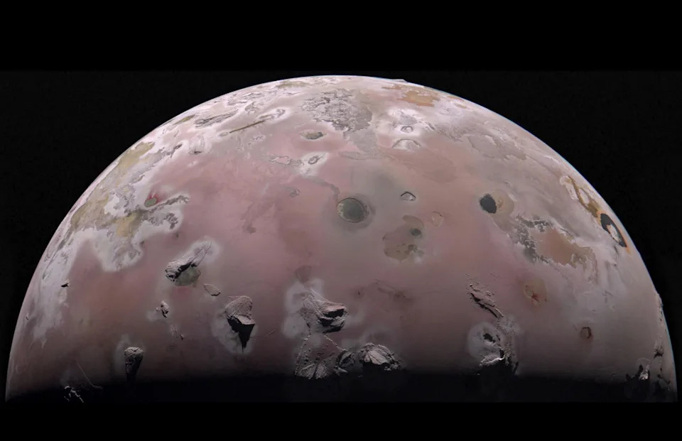 A close up of the planet Io, its pinkish surface dotted with dark spots and ridges