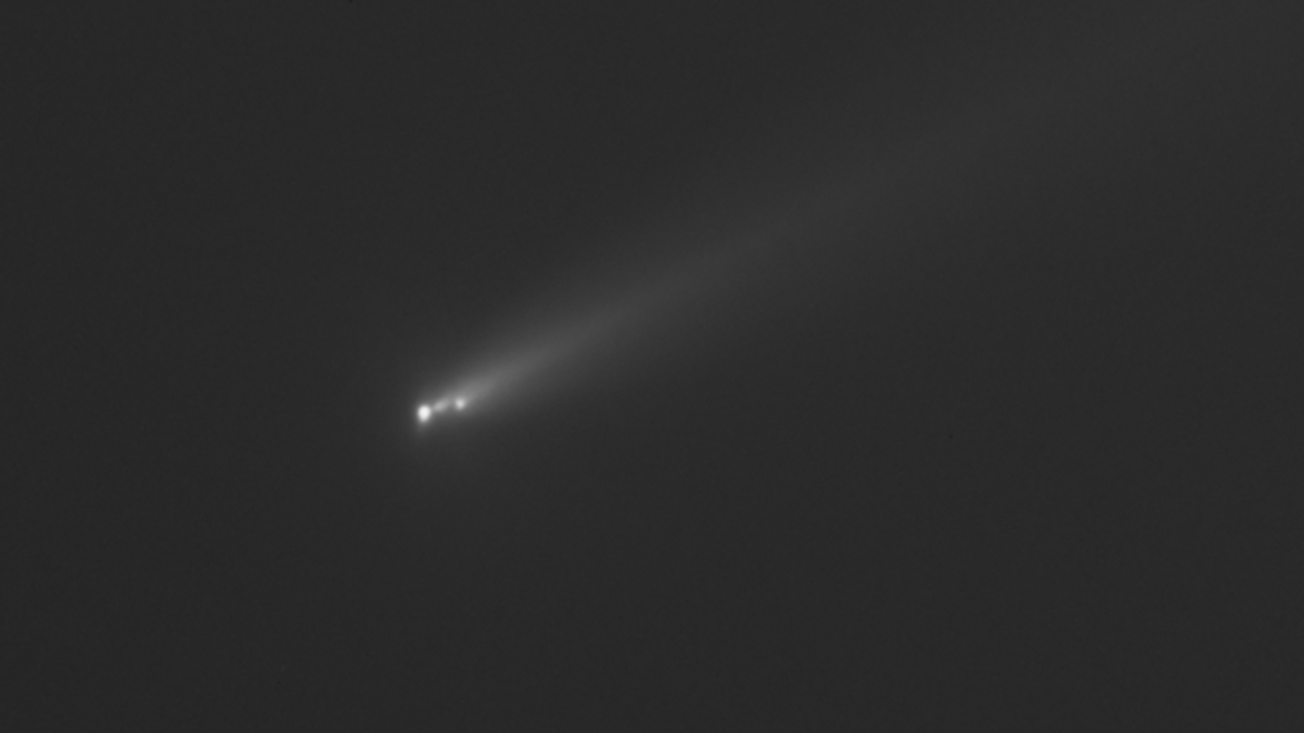 Three bright points of white light are pictured against a dark background representing the nucleus of a fractured comet, with a diffuse, hazy tail streaming away to the upper right of the image.