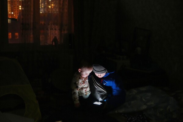 Daniil Dolotov, 11, plays on a phone with his brother Bohdanchyk, 18 months, in their apartment during a power outage caused by Russia’s repeated air strikes on the country’s power grid, in Kyiv, Ukraine, Monday, Feb. 2, 2026. (AP Photo/Sergey Grits)