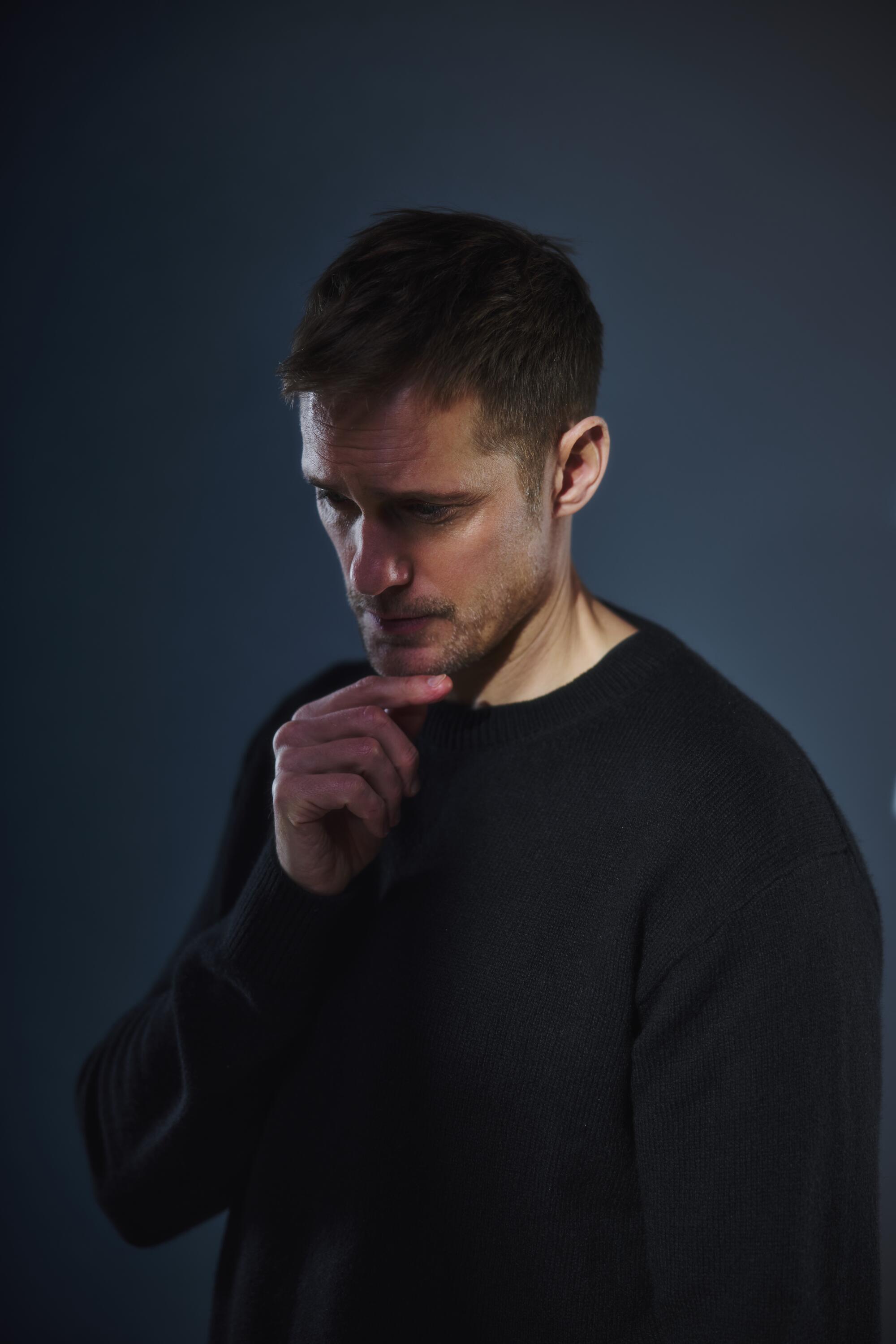 A man in a dark top touches his chin with his hand.