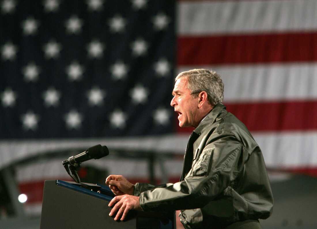 Standing behind a lectern equipped with two microphones, President George W. Bush delivers a speech inside an aircraft hangar at Elmendorf Air Force Base in Anchorage, Alaska, on Nov. 14, 2005.