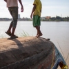 Two children stand on top of an overturned boat along a bank of the Mekong Delta.