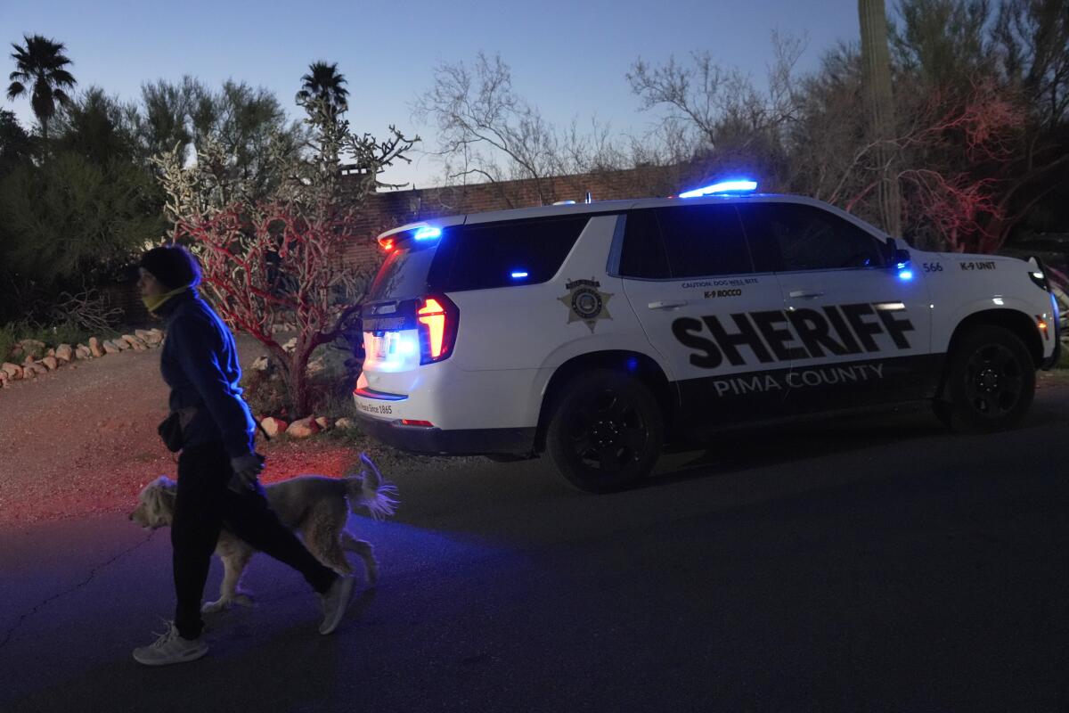 A woman walks her dog past a Pima county sheriff's vehicle parked in front of Nancy Guthrie's home