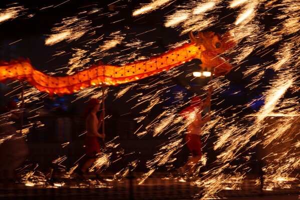 Fire performers carry a dragon during a molten iron fireworks performance known as "fire dragon steel flowers" ahead of Lunar New Year celebrations at an amusement park on the outskirts of Beijing, China, Saturday, Feb. 14, 2026. (AP Photo/Vincent Thian)