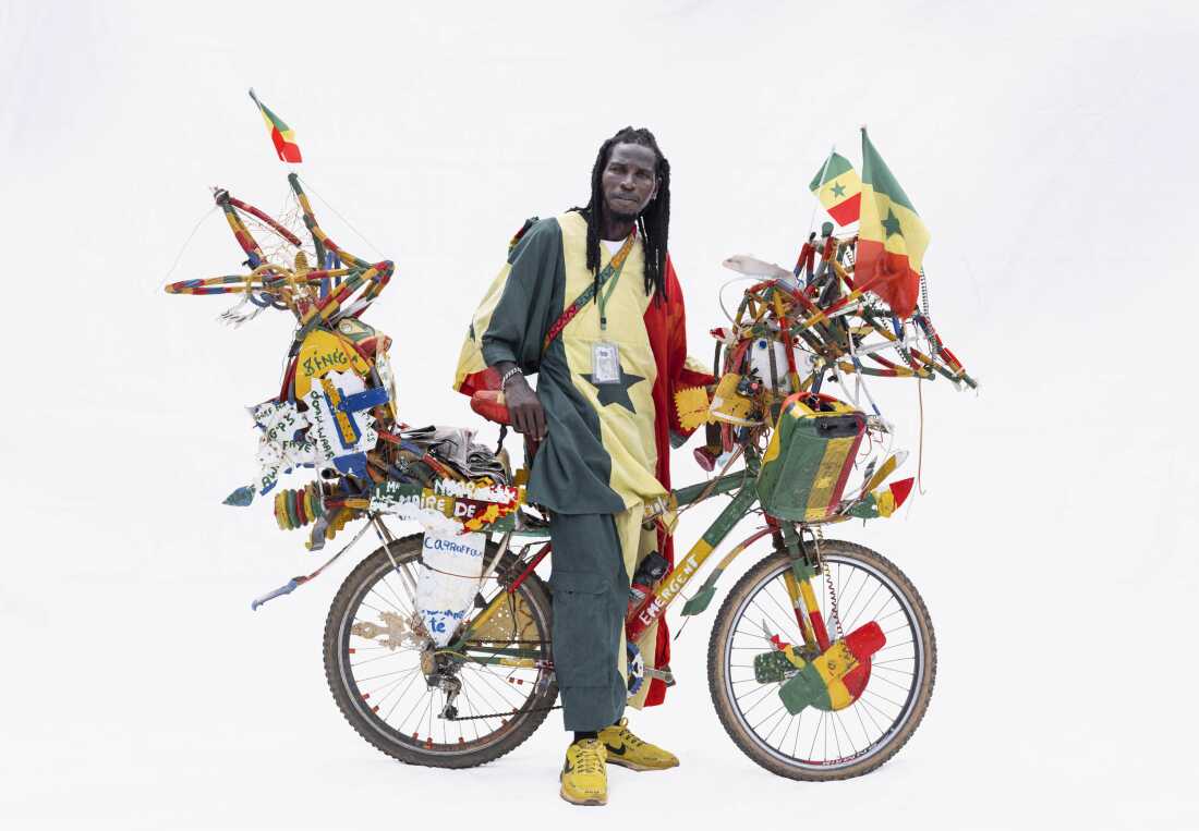 Mbaye, standing by his bicycle, is an artist and newspaper vendor in Ngaparou, Senegal.     