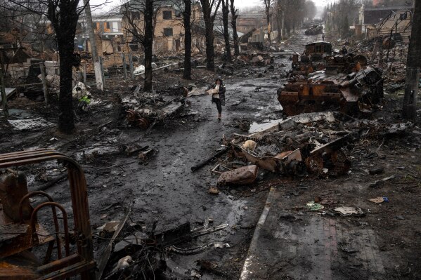 A woman navigates a debris-filled street where destroyed Russian military vehicles stand in Bucha on the outskirts of Kyiv, Ukraine, Sunday, April 3, 2022. (AP Photo/Rodrigo Abd, File)