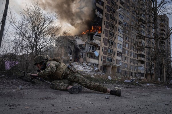 A Ukrainian police officer takes cover in front of a burning building that was hit in a Russian airstrike in Avdiivka, Ukraine, Friday, March 17, 2023. (AP Photo/Evgeniy Maloletka, File)