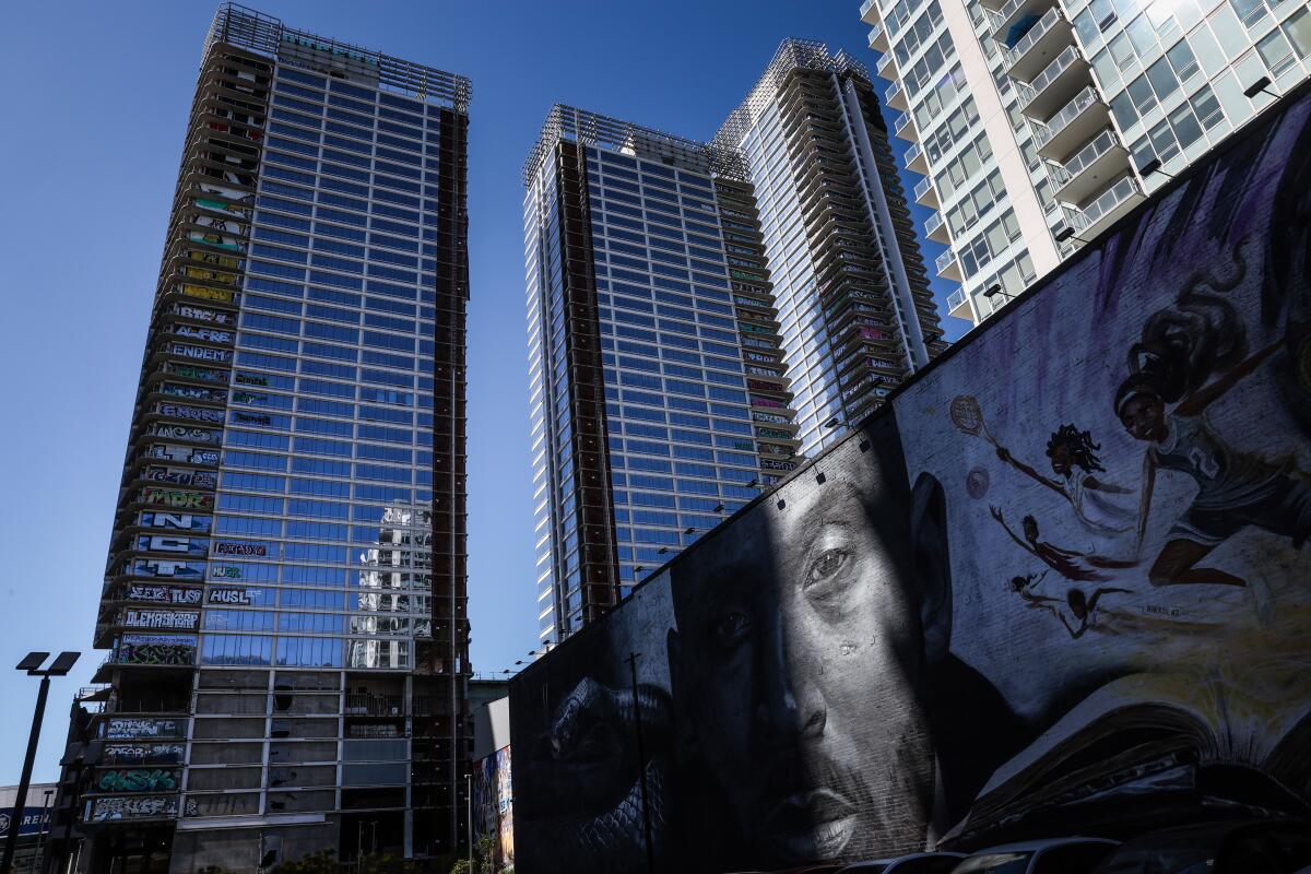 A view of skyscrapers, two bearing graffiti on every floor, with a large mural of a man on the lower right