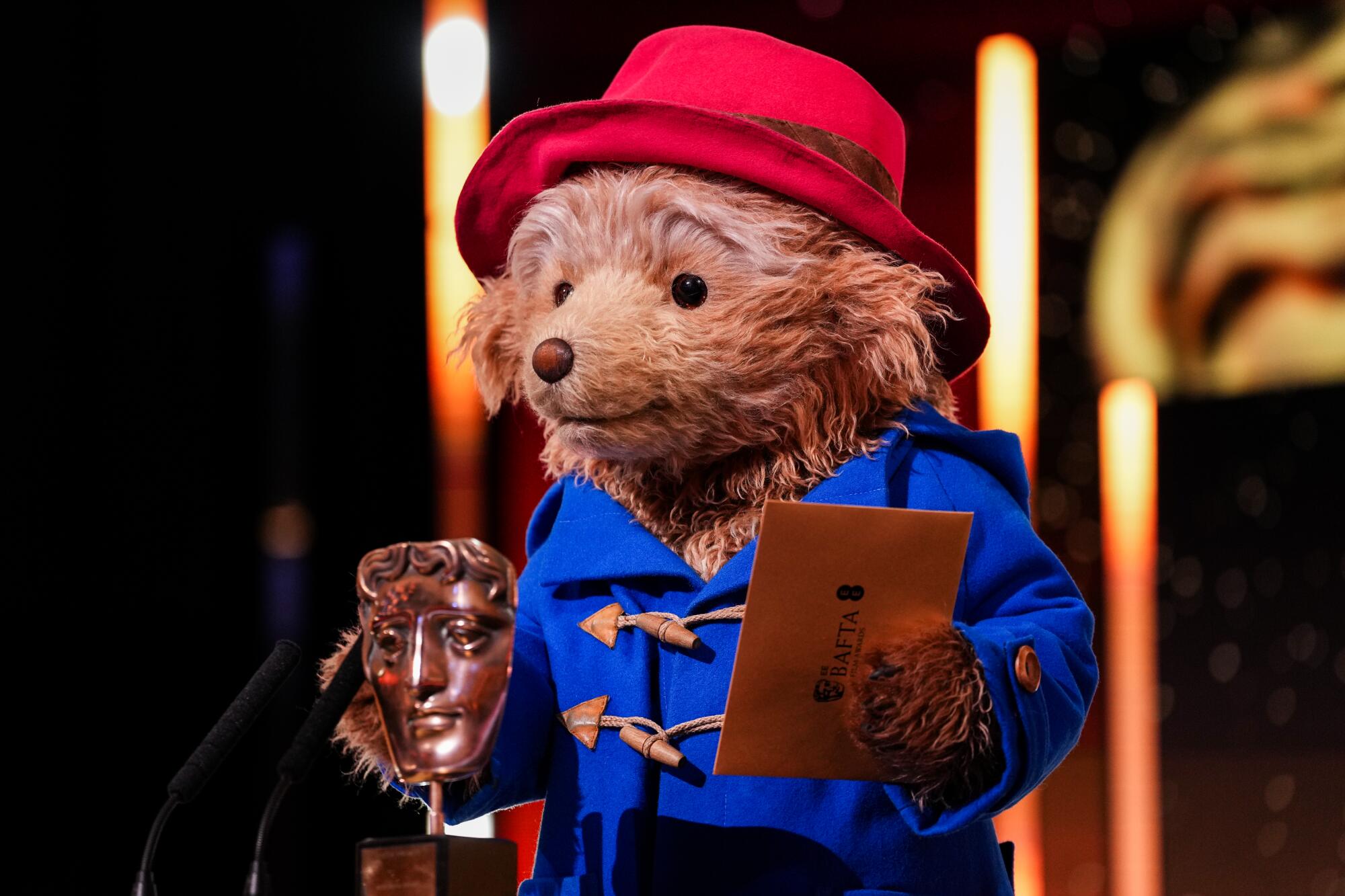 A bear in a red hat stands at a podium at an awards show.
