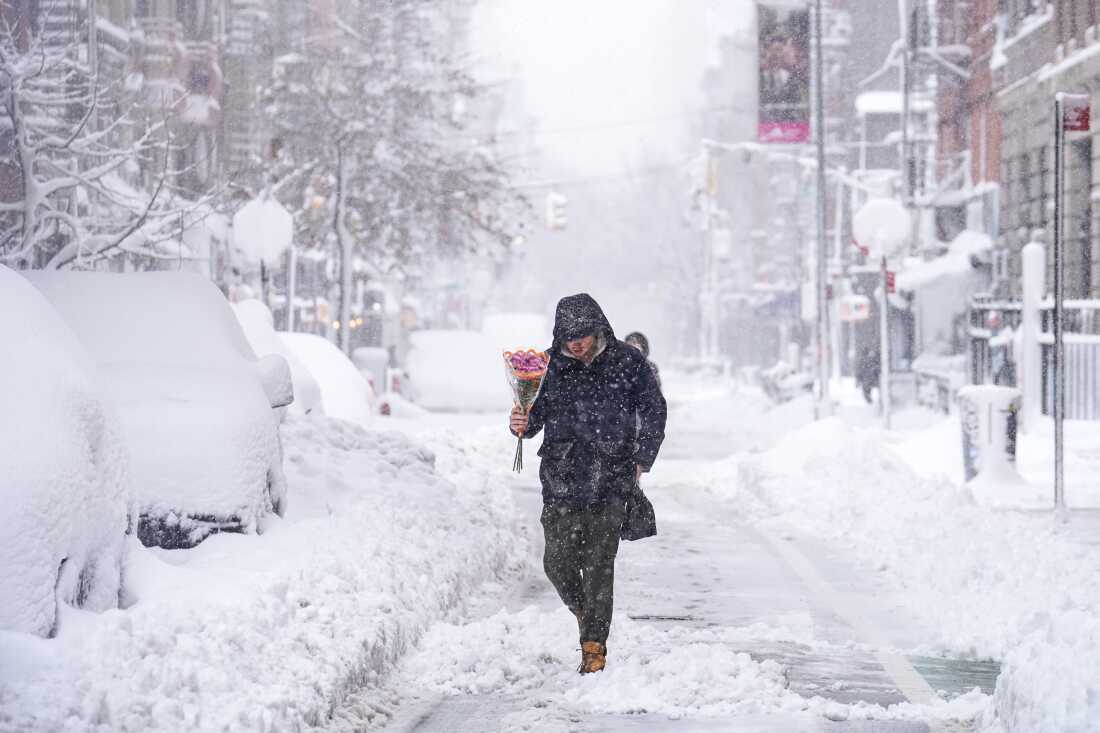 A person carrying flowers walks through the snow in the Lower East Side on February 23, 2026 in New York City.