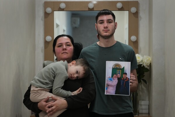 Oksana Osypenko, 43, her sons Davyd, right, and Hlib, 5, pose with a photograph, Thursday, Feb. 19, 2026, in Kyiv, Ukraine, taken before Russia's full-scale invasion showing her husband, Oleksandr, who was killed in an airstrike. (AP Photo/Sergei Grits)