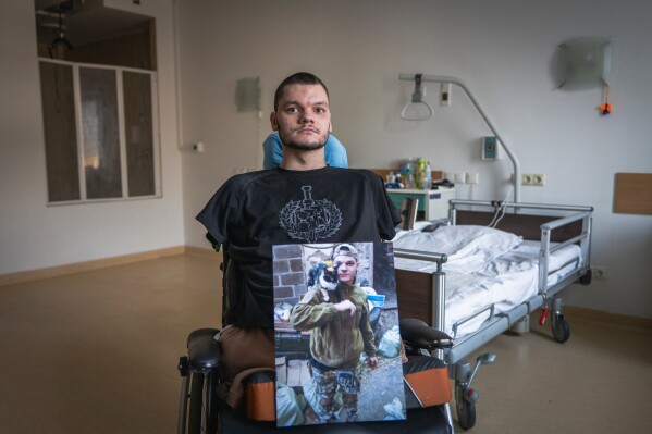 Ruslan Knysh, 20, a war veteran, sits in a wheelchair with a photograph of himself taken before he lost his limbs in a drone attack last year, in Kyiv, Ukraine, Sunday, Feb. 22, 2026. (AP Photo/Dan Bashakov)