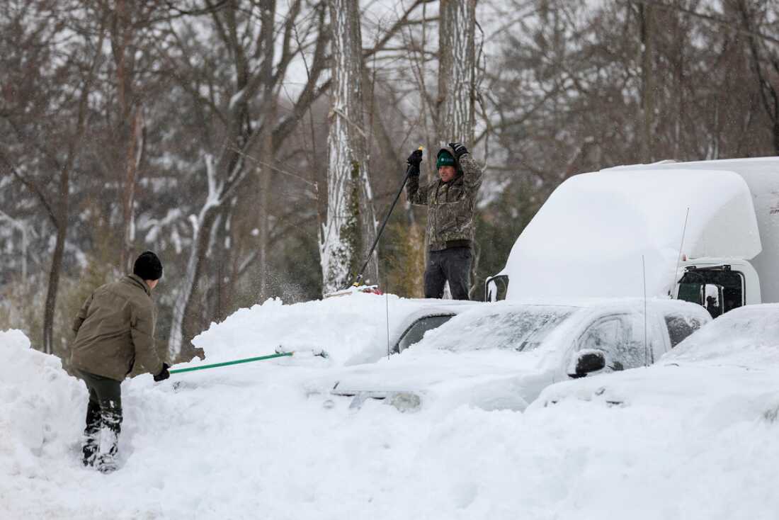 Men clear snow off of cars and trucks on Monday in a parking lot in St. James, N.Y.