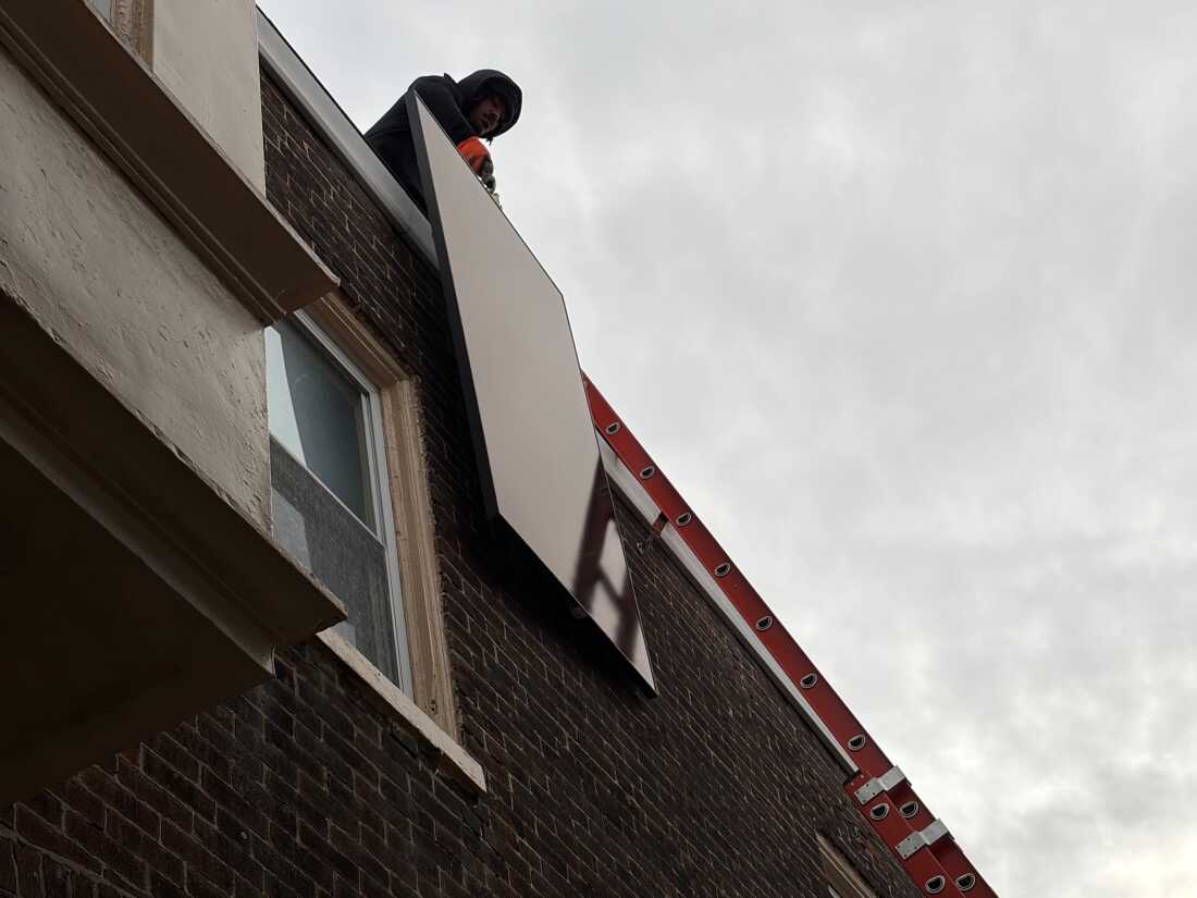 A Solar States installation crew hoists a solar panel onto the roof of a Philadelphia home.