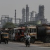 A motorcyclist and a three-wheel tuk-tuk pass a line of oil tanker trucks parked outside an oil refinery.