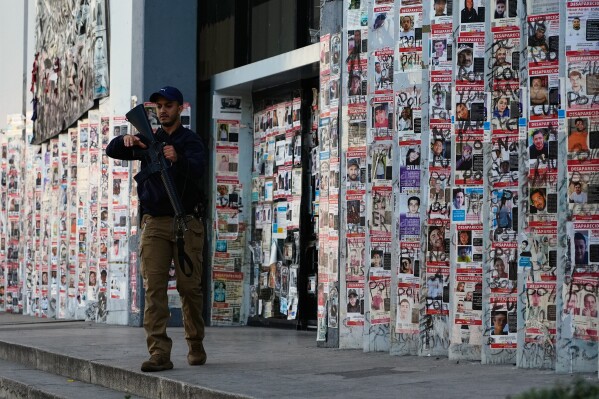 A police officer walks past posters of missing persons in front of the Special Prosecutor's Office for Missing Persons in Guadalajara, Mexico, Wednesday, Feb. 25, 2026. (AP Photo/Marco Ugarte)