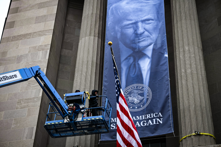 Image: Workers install a new banner featuring an image of President Donald Trump on the facade of the U.S. Department of Justice