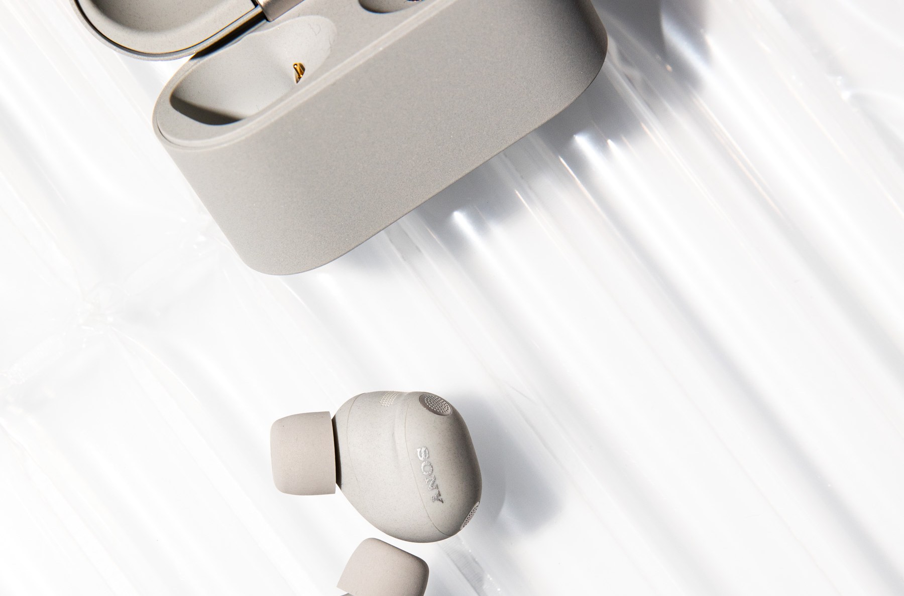 The Sony WF-1000XM6 earbuds and open case in light gray on a textured off-white background.
