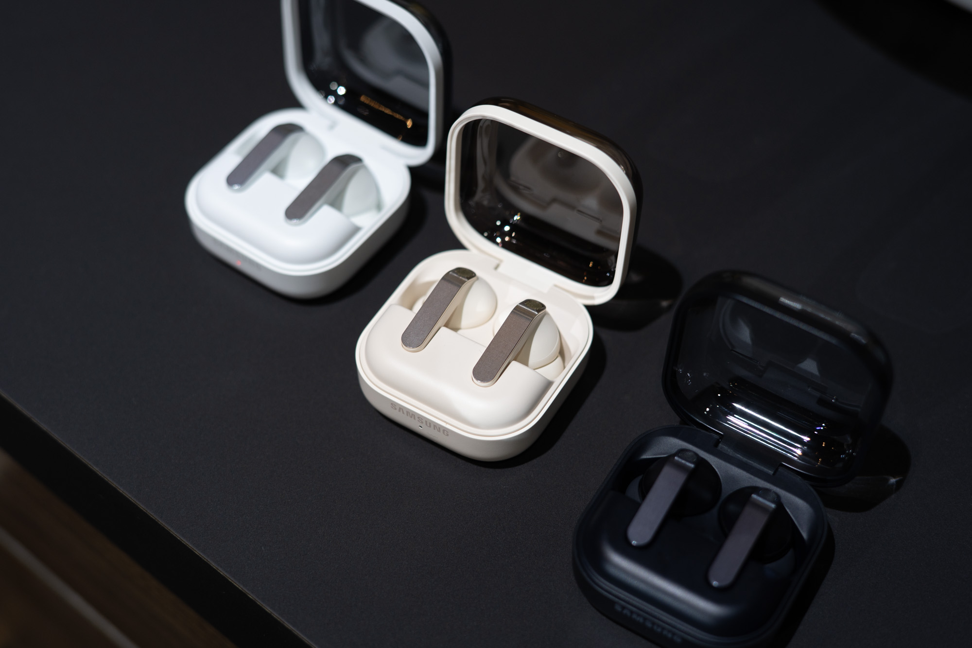 Samsung Galaxy Buds 4 Pro in white, pink, and black with open cases on a black surface