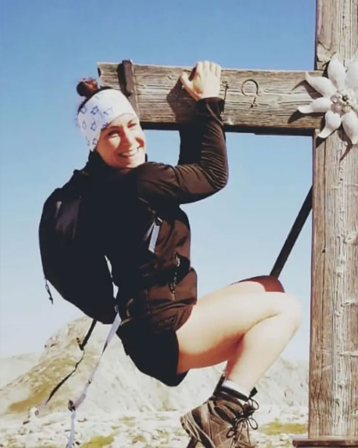 Climber hanging from wooden cross on mountain, smiling and wearing hiking gear and headband under clear blue sky. Climber hanging from wooden cross on mountain, smiling and wearing hiking gear and headband under clear blue sky.