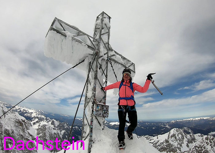 Climber standing on snowy mountain peak next to large icy cross during an alpine expedition in Dachstein. Climber standing on snowy mountain peak next to large icy cross during an alpine expedition in Dachstein.