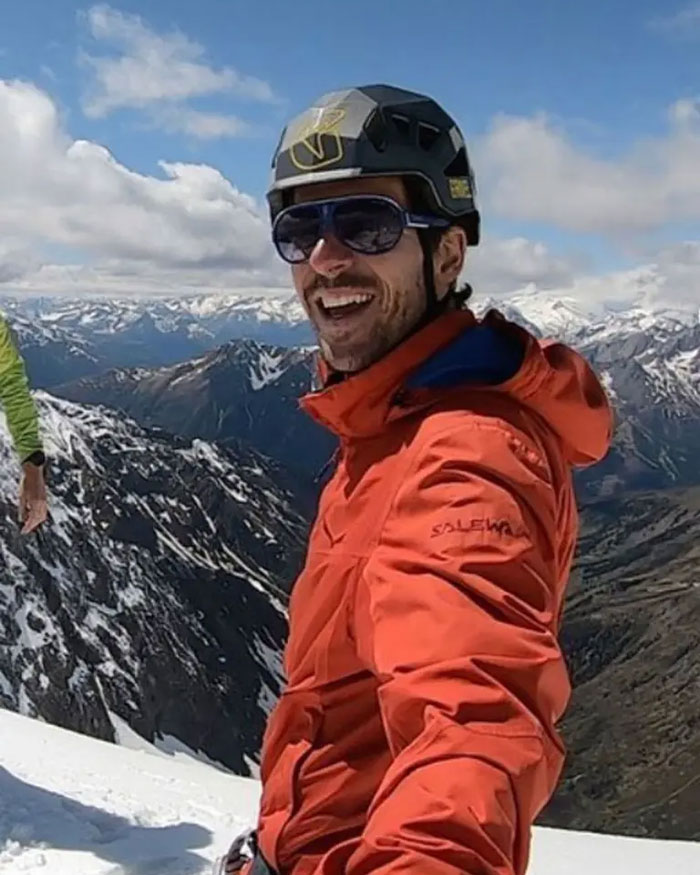 Climber wearing helmet and sunglasses on snowy mountain with scenic valley in background, revealing heartbreaking last words. Climber wearing helmet and sunglasses on snowy mountain with scenic valley in background, revealing heartbreaking last words.