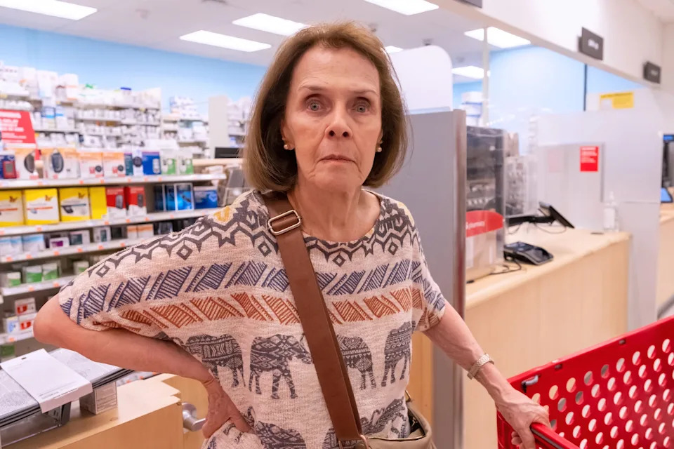 Woman in a store with a shopping cart, wearing a patterned elephant-print shirt, looking directly at the camera