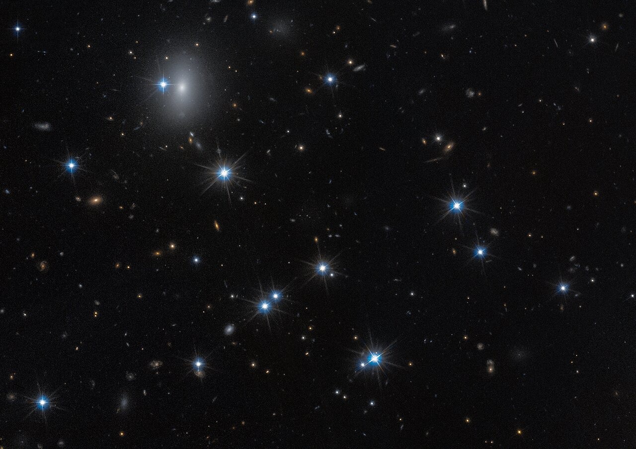 A field of space with a dozen white foreground stars and a number of small, yellow background galaxies