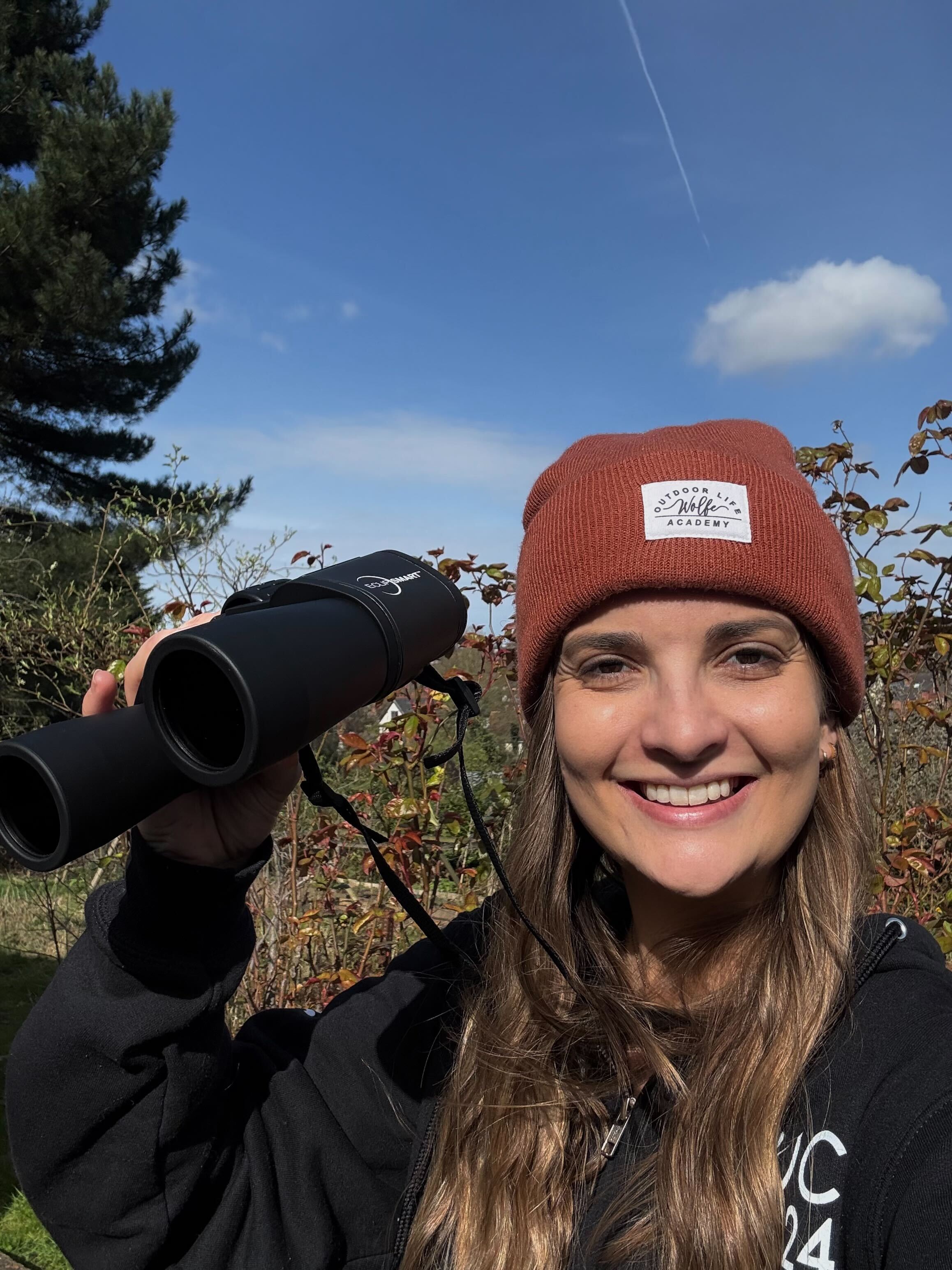 A woman holding solar binoculars and smiling during a partial solar eclipse.