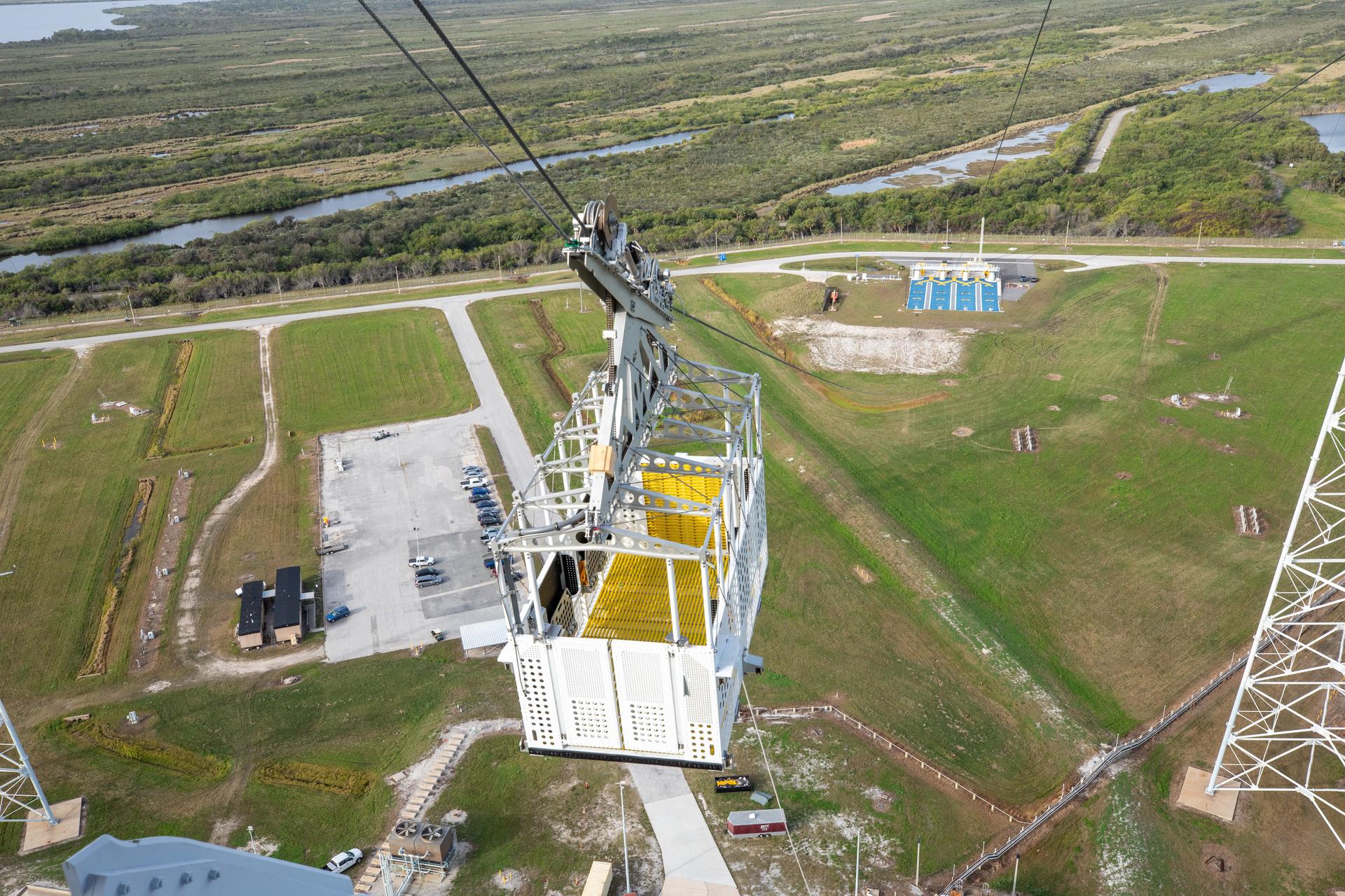 The emergency egress system, seen during installation of the baskets in January 2024. The landing zone, a royal blue rectangle, is visible in the background at ground level.