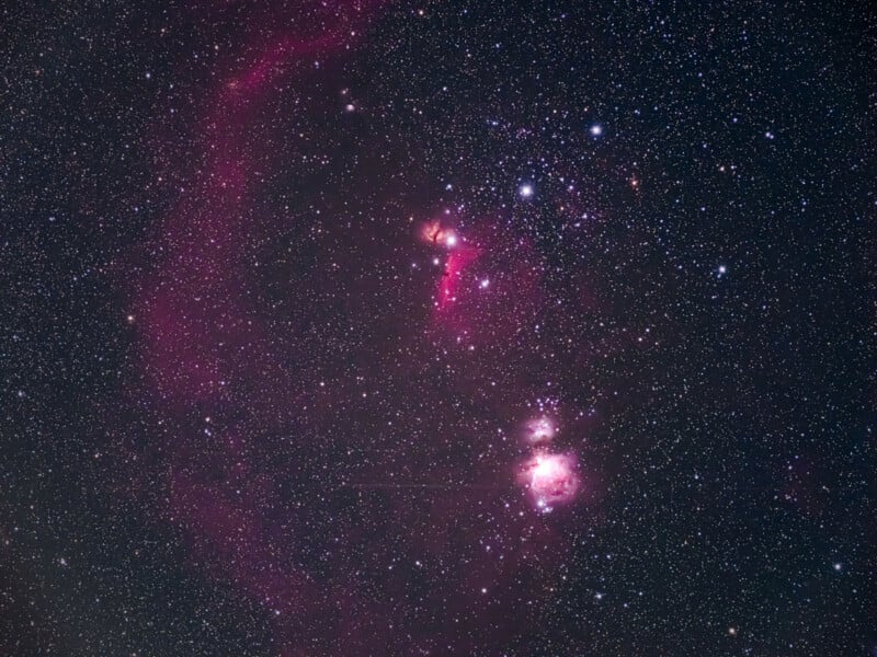 A star-filled night sky featuring the Orion constellation, with bright stars and a pinkish nebula visible among countless smaller stars scattered across the dark expanse.