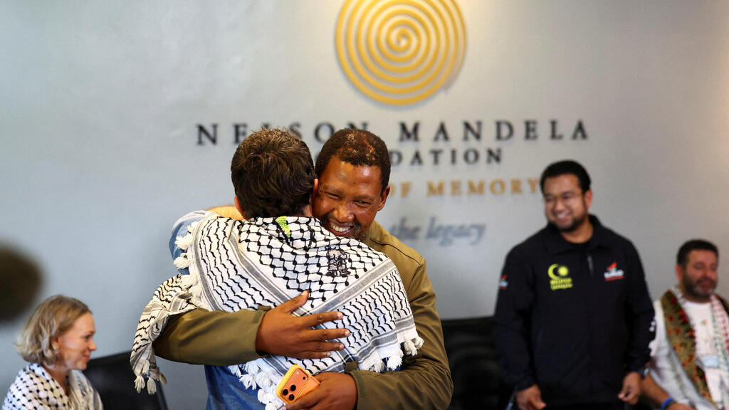 Mandela’s grandson embraces an activist wearing a keffiyeh at the news conference (Photo: REUTERS/Siphiwe Sibeko) מנדלה מנדלה נכדו של נלסון מנדלה במסיבת עיתונאים של פעילים אנטי-ישראליים ב יהונסבורג דרום אפריקה שבה הכריזו על משט חדש ל עזה