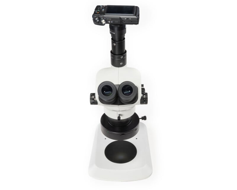 A white laboratory microscope with dual eyepieces and a digital camera attached to the top, viewed from above on a white background.