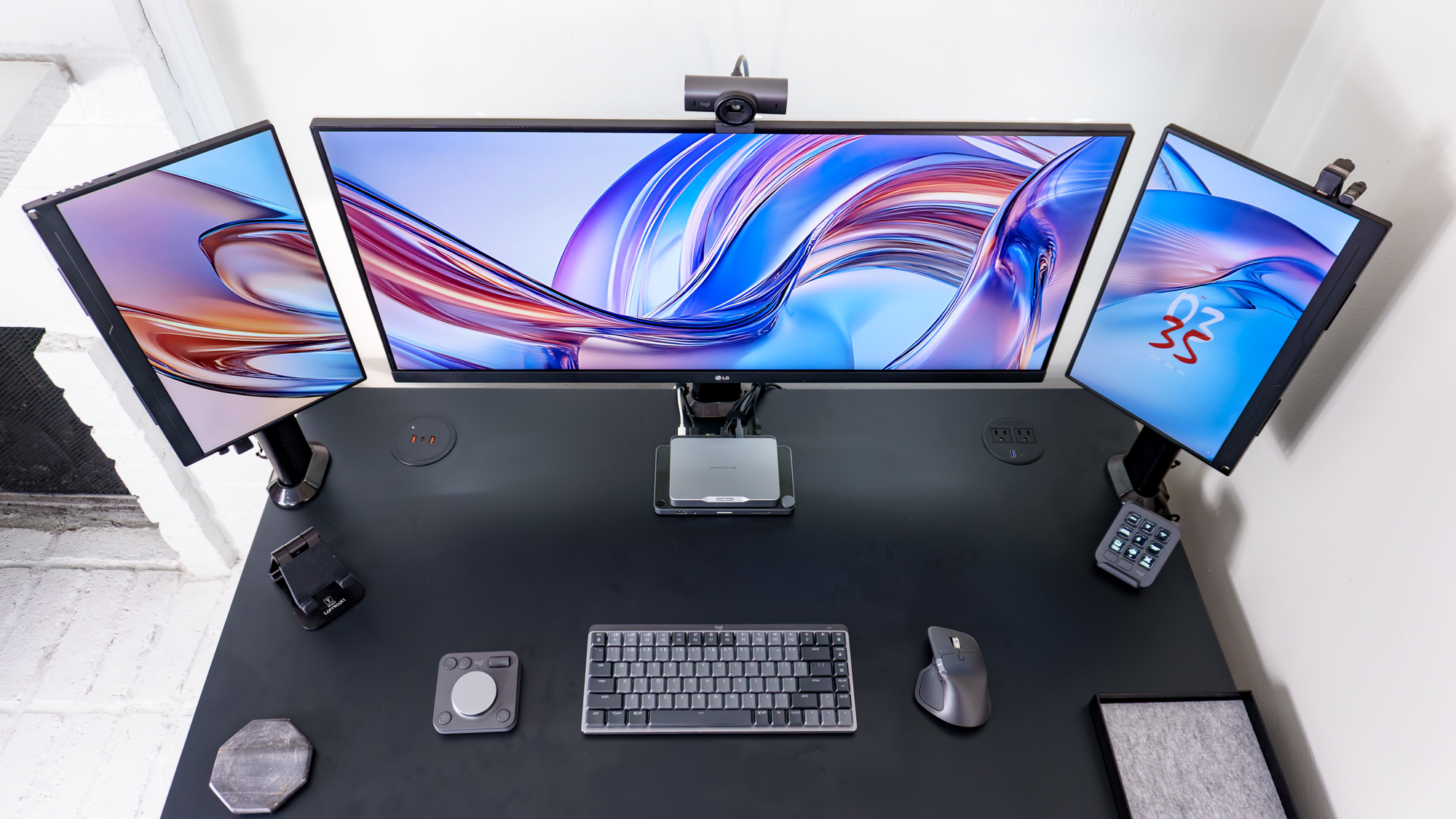 An overhead view of a less conventional triple monitor setup with peripherals from Logitech's MX Master Series on the desk