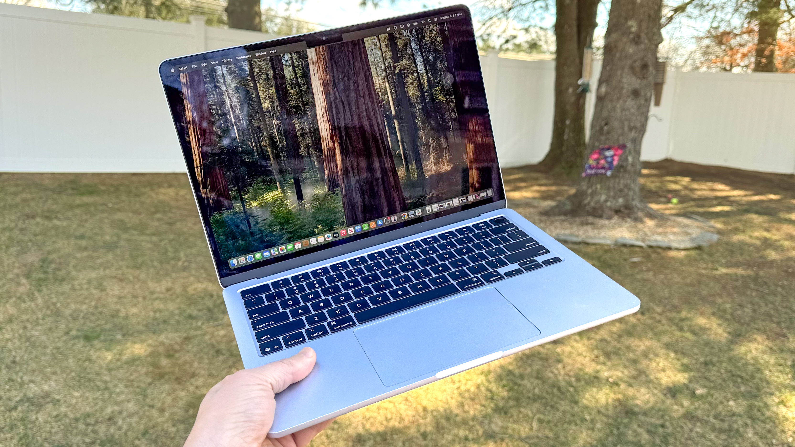 Person holding the MacBook Air 13-inch M4 outside above grass in a shaded garden