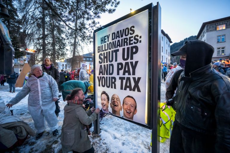 A banner bearing portraits of Elon Musk, Jeff Bezos and Mark Zuckerberg with a slogan is seen during a demonstration against the World Economic Forum (WEF) on the eve of the WEF annual meeting in Davos on January 18, 2026. (Photo by Fabrice COFFRINI / AFP)