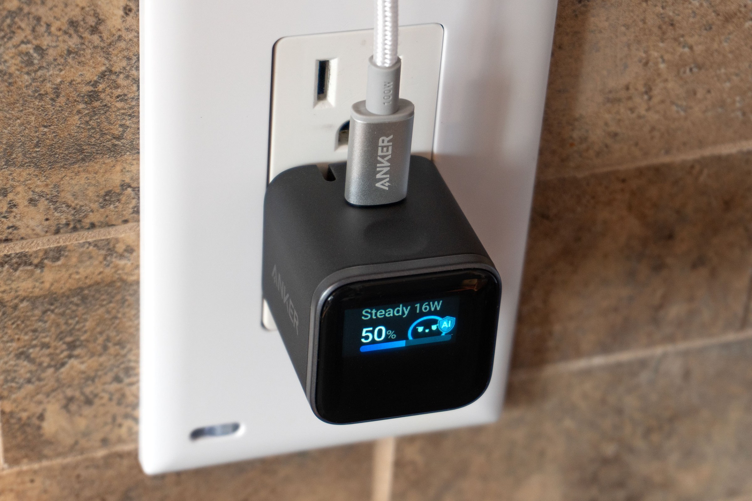 A closeup of the Anker Nano Charger plugged into a wall outlet showing a touch-sensitive indented button on top.