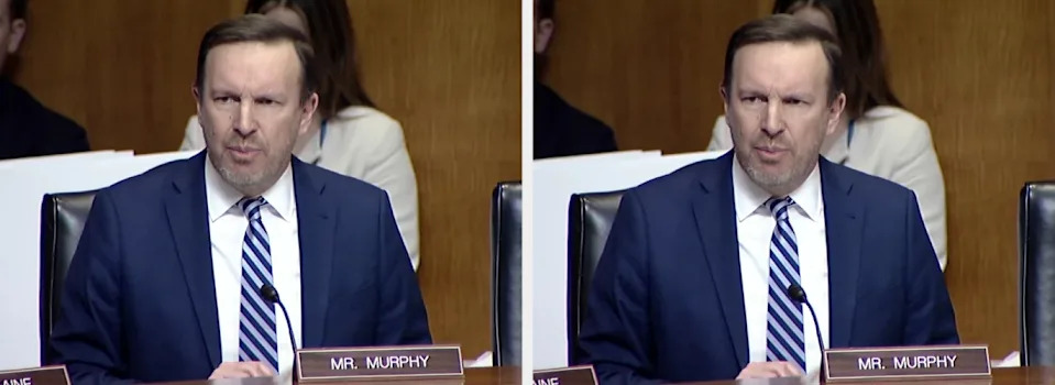 A person in a suit and tie speaks at a formal event, sitting at a table with a nameplate marked "Mr. Murphy."