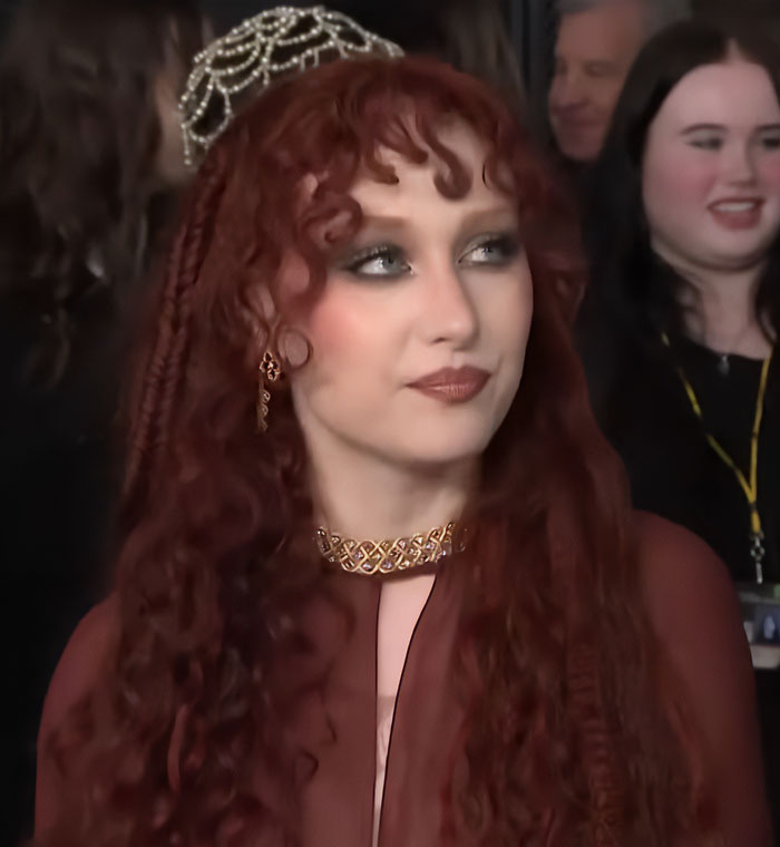 Chappell Roan with red curly hair and ornate jewelry at an event following Grammys look controversy. Chappell Roan with red curly hair and ornate jewelry at an event following Grammys look controversy.