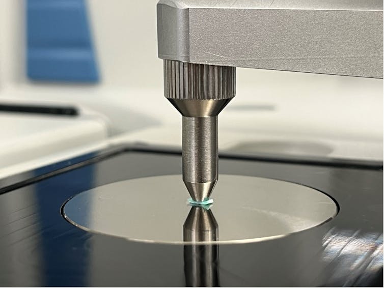 Close-up of a steel instrument with a probe placed on a small piece of green plastic.