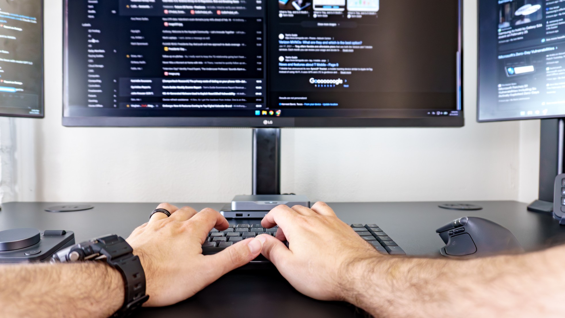 A person typing on the Logitech MX Mechanical Keys Mini at a triple monitor setup with a MX Master 4 mouse on the right and the MX Creative Dialpad on the left