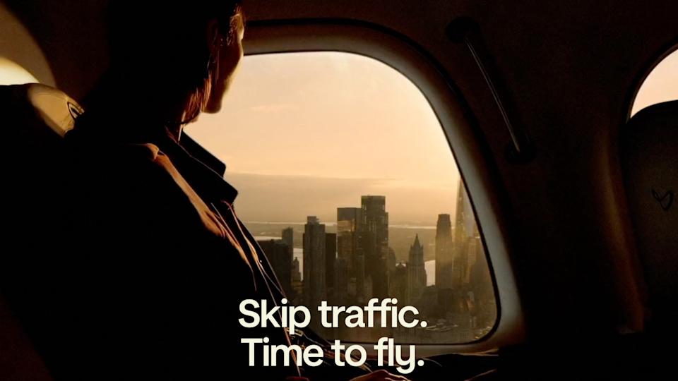 A person looks out the window of an air taxi, viewing the city below.