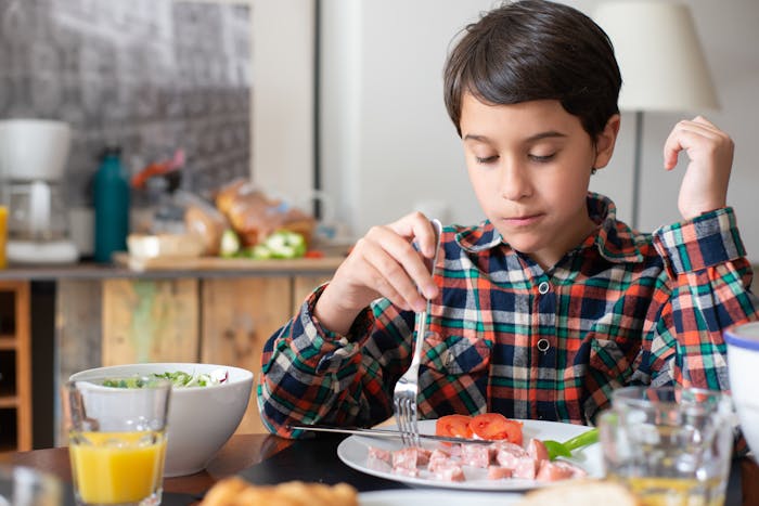 Young boy eating breakfast alone at kitchen table, illustrating parenting and family conflict themes.