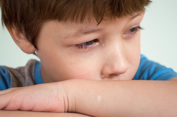 Sad young boy with tear on his cheek, reflecting on family conflict involving parenting and brother’s interference.