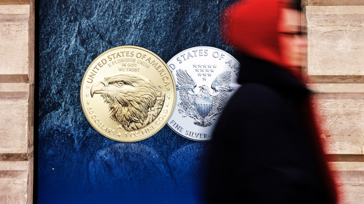 A person walks past a poster of gold and silver bullion coins.