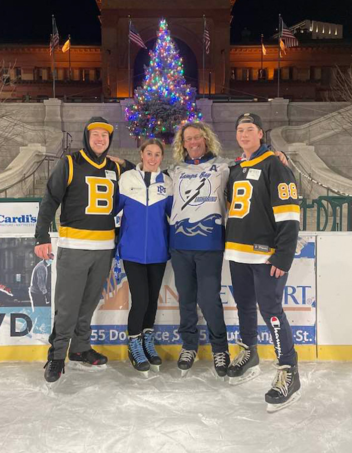 Group of four people ice skating at night with a decorated Christmas tree in the background at an ice rink setting. Group of four people ice skating at night with a decorated Christmas tree in the background at an ice rink setting.